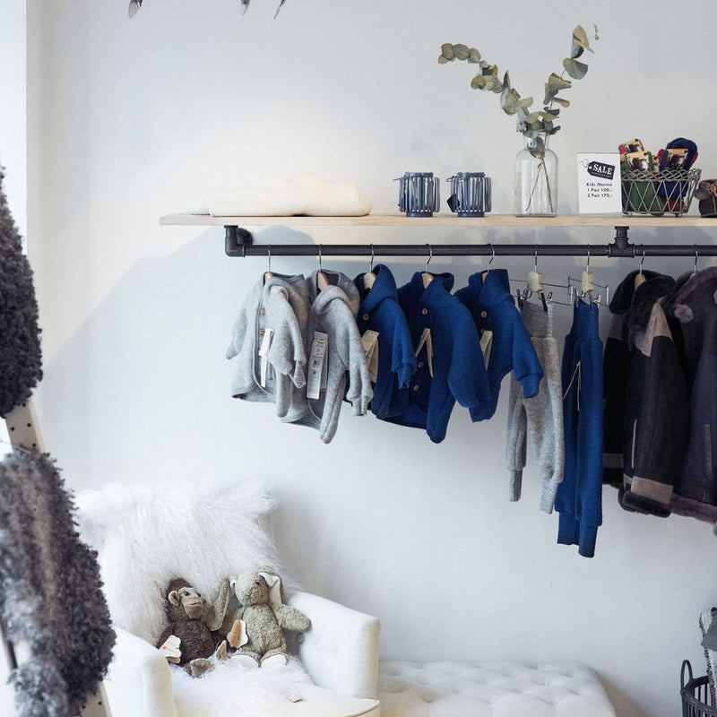 Wandmontiertes Regal mit Kleiderstange mit dunklen Wasserrohren und Kiefer in Geschäft für Babykleidung